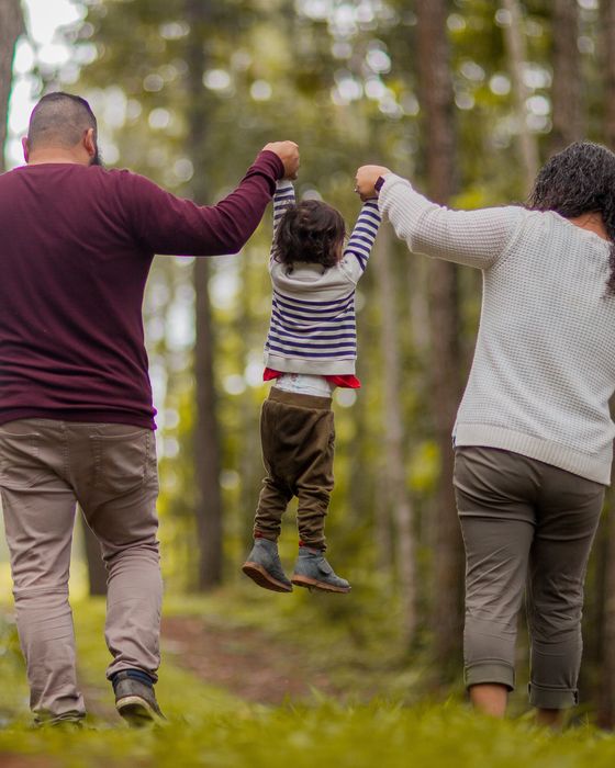 Parents swinging their toddler between them on a forest path